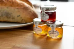 A close-up of a wooden kitchen worktop with bread and several small jars of food or preserves.
