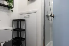 A modern bathroom with a shower enclosure, toilet, wall-mounted towel rail and wooden-effect flooring.