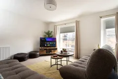 A comfortable lounge with sofas, armchairs, a coffee table, cushions and a TV in the far corner.