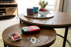 A close-up of a round coffee table with drinks, a bowl of snacks and several small decorative items such as the UNO card game.