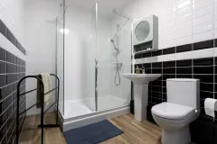 A modern bathroom with a glass shower enclosure, toilet, wall-mounted basin and black and white tiled walls.