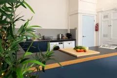 A close-up of a modern kitchen worktop with a wooden chopping board, vegetables, plants and cream kitchen cabinets in the background.