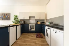 A modern kitchen with dark blue lower cabinets, cream wall cabinets, a central island, integrated appliances and wooden flooring.