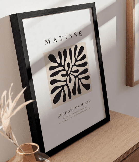 A close-up shot of the artwork displayed on a wooden desk, reflecting natural light. The sleek frame adds a sophisticated touch to a workspace or living area.