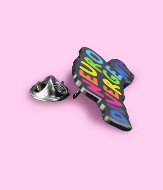 The same enamel pin is displayed on a pastel pink background with its butterfly clutch backing shown separately, illustrating its secure fastening mechanism.