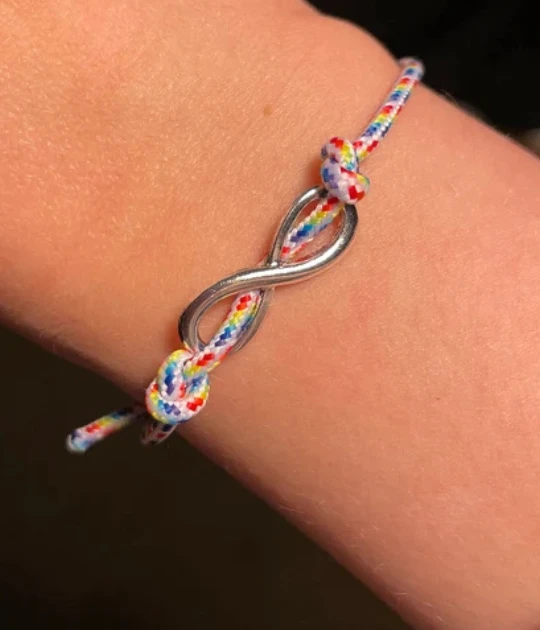A close-up of the bracelet worn on a person’s wrist showcases the silver infinity charm and colorful braided design, emphasizing its lightweight and adjustable fit.