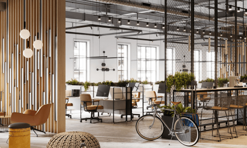 Modern open-plan office with shared desks, plants, and industrial design details including a bicycle, warm lighting, and partitions.